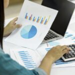 A businesswoman uses a calculator to check data graphs.