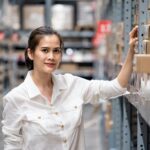 Smart Asian young woman standing and checking quality and quantity of inventory stock on shelf