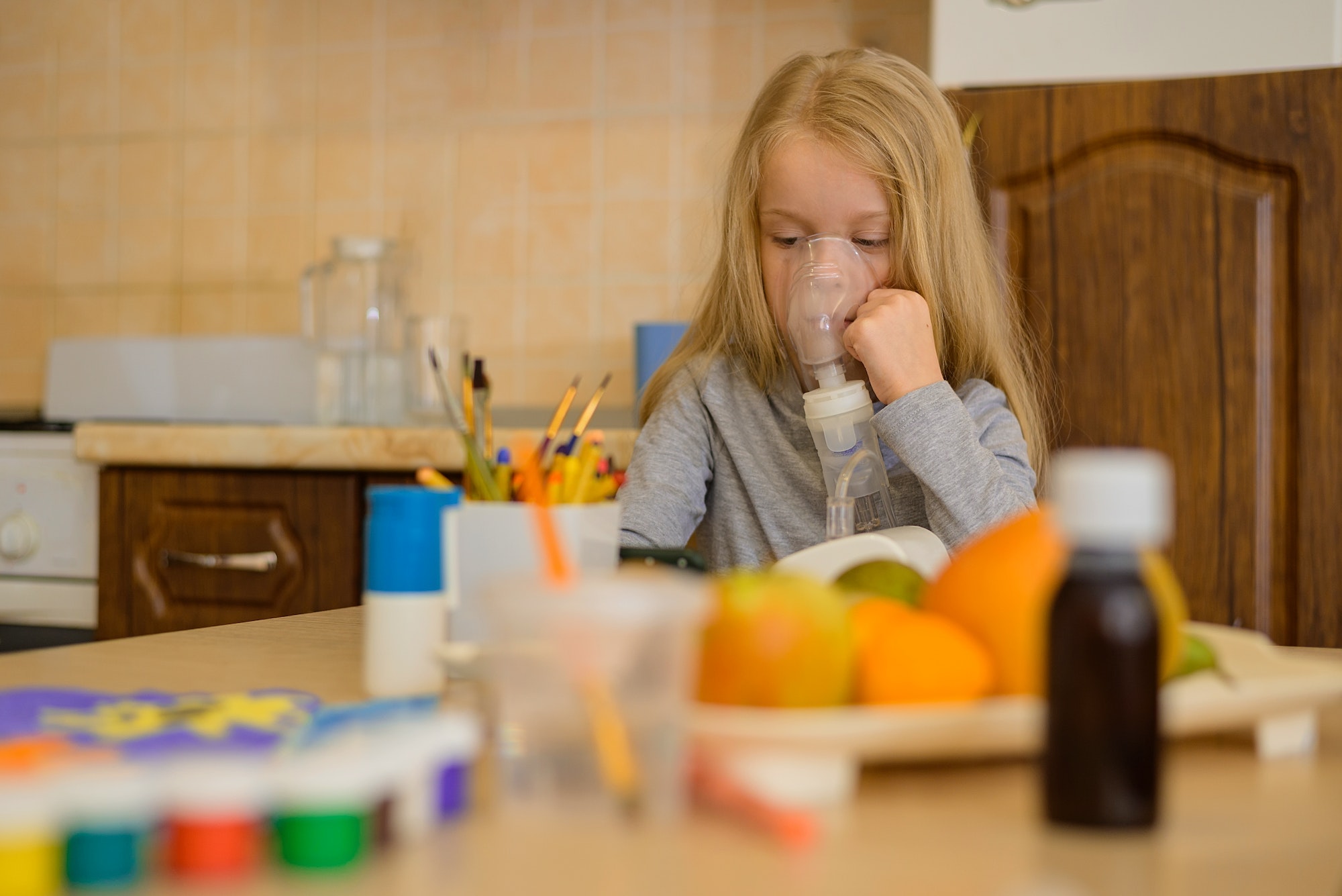 child at home sits at a table and makes inhalation with a nebulizer, watching cartoons on the phone